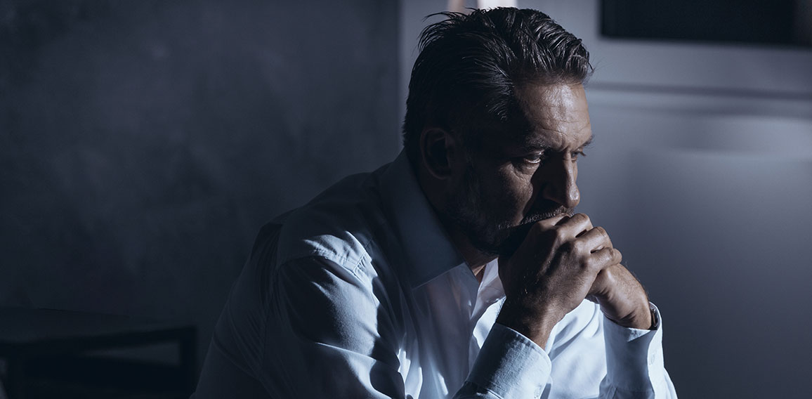 Portrait of a lonely mature man with depression sitting on a bed