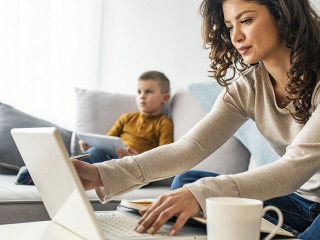 Smiling mom working at home with her child on the sofa while wri