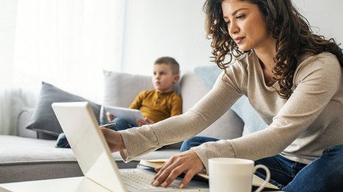 Smiling mom working at home with her child on the sofa while wri