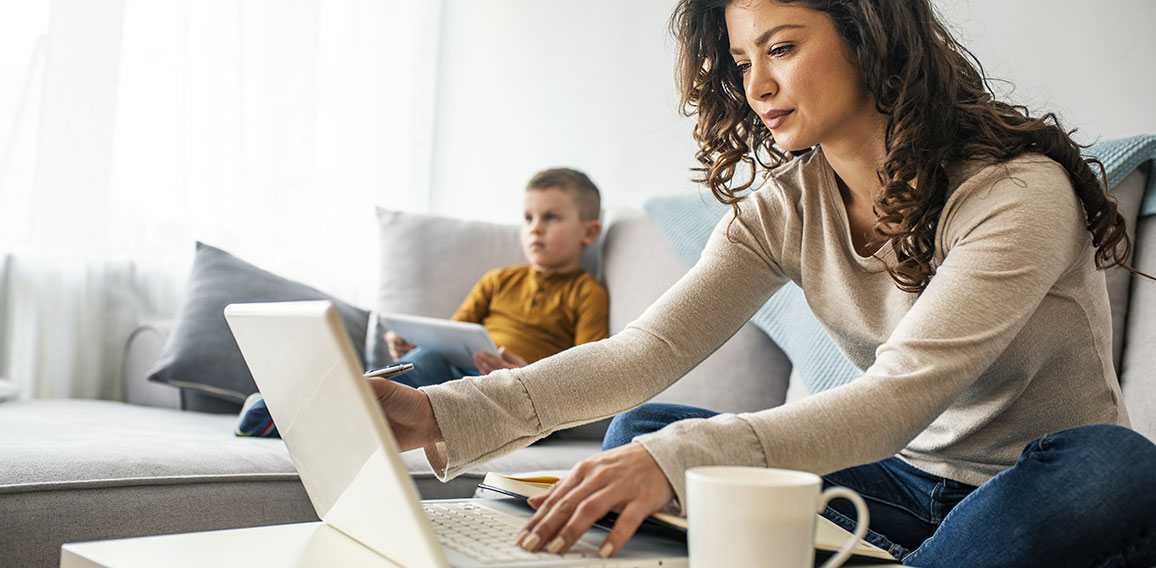 Smiling mom working at home with her child on the sofa while wri