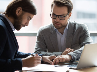Focused young businessman signing agreement with skilled lawyer.
