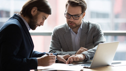 Focused young businessman signing agreement with skilled lawyer.