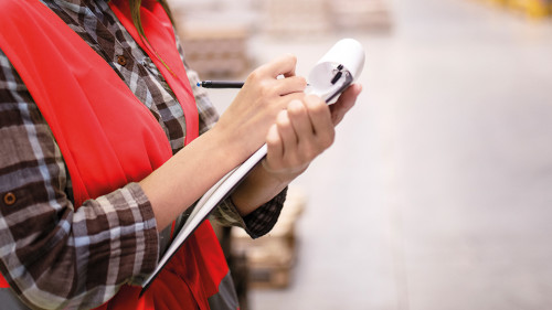 Woman warehouse worker leaning on cardboard boxes and taking not