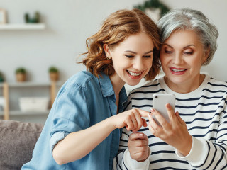 Cheerful mother and daughter using smartphone on sofa