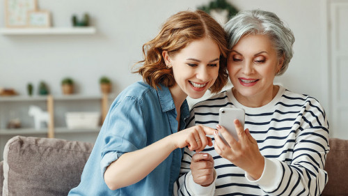 Cheerful mother and daughter using smartphone on sofa