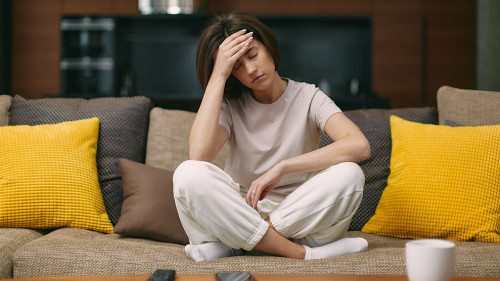 Sick young girl suffering headache or migraine, sitting on sofa at home, feel pain of sore head, morning after hangover