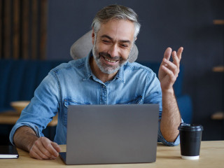 Portrait of grey-haired senior handsome smiling man working from home. Communication online with colleagues and video conference. Online meeting, video call, remote working