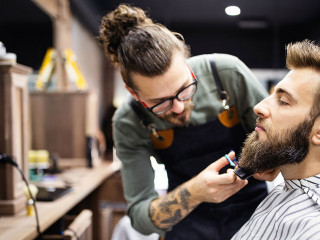 Happy young handsome man visiting hairstylist in barber shop salon