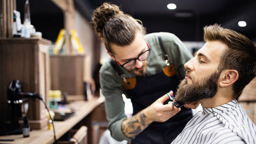 Happy young handsome man visiting hairstylist in barber shop salon