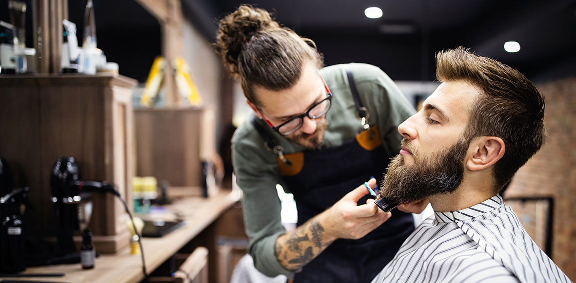 Happy young handsome man visiting hairstylist in barber shop salon