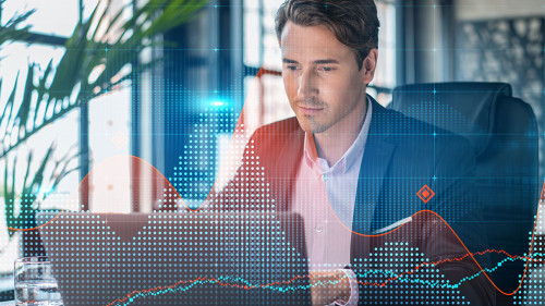 Handsome businessman in suit at workplace working with laptop to optimize trading strategy at corporate finance fund. Forex chart hologram over office background