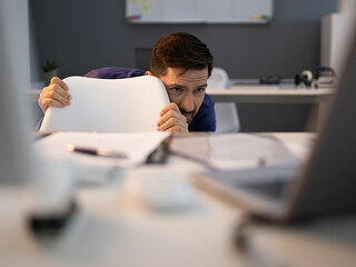 Frightened Businessman Hiding Behind Chair