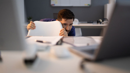 Frightened Businessman Hiding Behind Chair