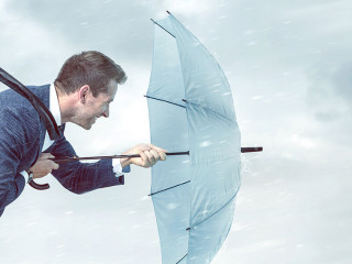 Businessman with an umbrella is facing strong headwind