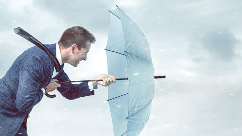 Businessman with an umbrella is facing strong headwind