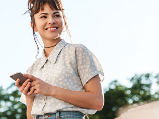 Positive cheery happy young beautiful woman on a balcony using mobile phone chatting.