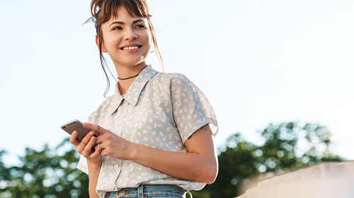 Positive cheery happy young beautiful woman on a balcony using mobile phone chatting.