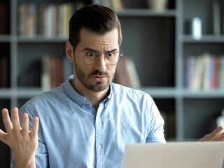 Unhappy young man work on laptop confused by gadget problems