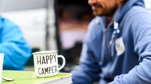 Man camping travelling with breakfast mug and happy camper text.