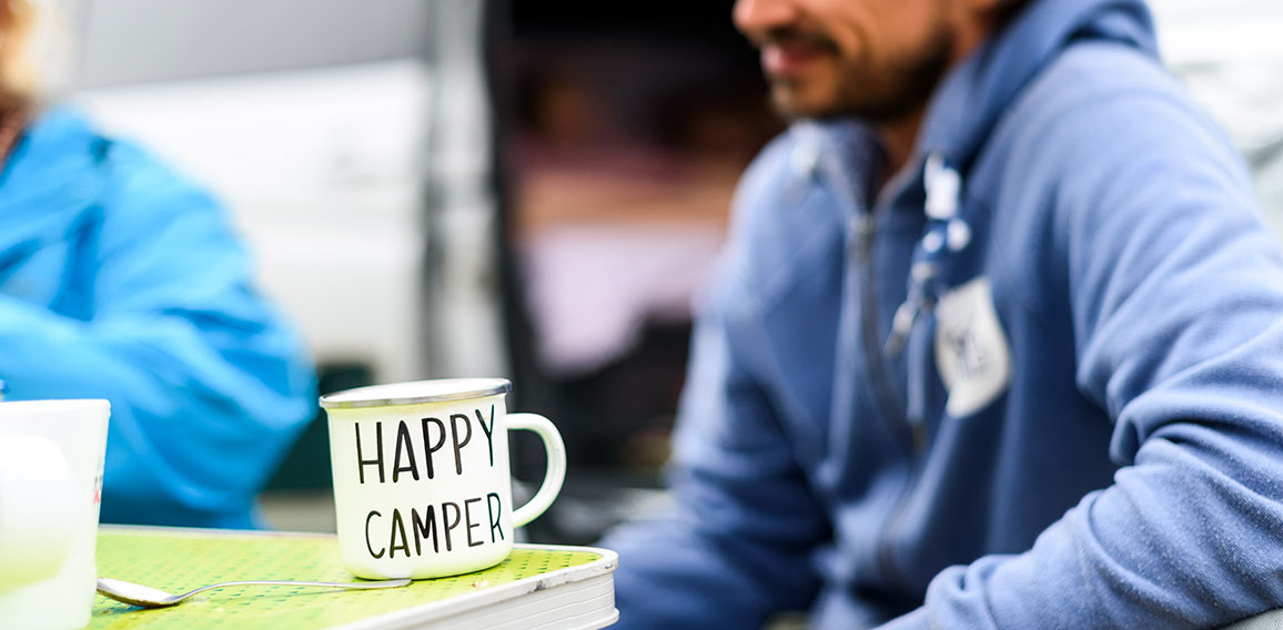 Man camping travelling with breakfast mug and happy camper text.