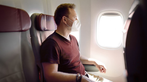 Middle age man in face mask traveling by an airplane. Passenger sitting in aircraft and looking on plane window during flight. Safety and protection of fly transportation while coronavirus