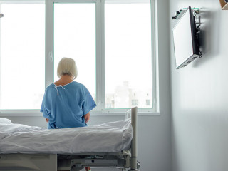 back view of lonely senior woman sitting on bed in hospital ward