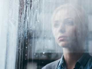 selective focus of sad adult woman at home looking through windo