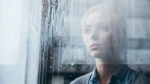 selective focus of sad adult woman at home looking through windo