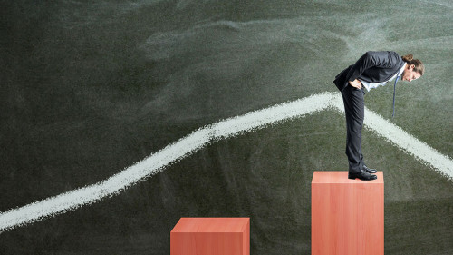 Businessman on red chart bars on chalkboard wall background. Crisis, business and growth concept.