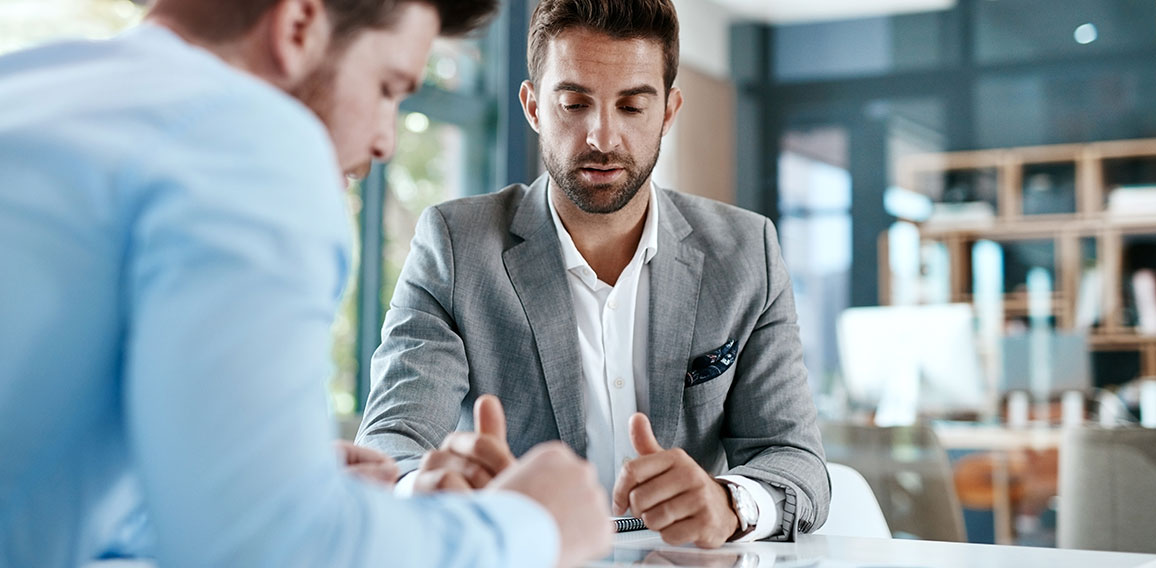 Digitizing a financial discussion. Cropped shot of two young businessmen using a digital tablet while going through paperwork together in a modern office.