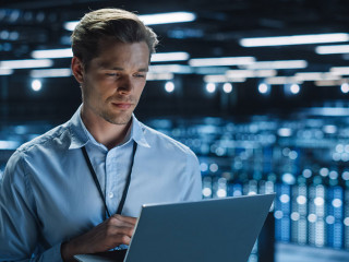 Handsome Smiling IT Specialist Using Laptop Computer in Data Cen