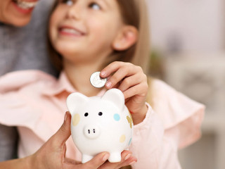Young girl and her mother with piggybank sitting at table