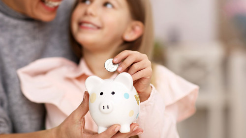 Young girl and her mother with piggybank sitting at table
