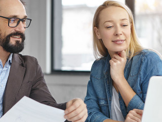 Successful mature bearded businessman and his colleague work together in office, discuss statistics. Young female shows presentation on laptop computer to her boss, going show it on business meeting