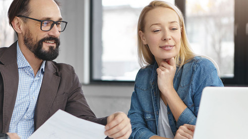 Successful mature bearded businessman and his colleague work together in office, discuss statistics. Young female shows presentation on laptop computer to her boss, going show it on business meeting