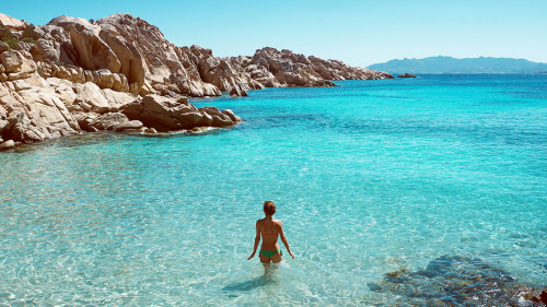 Frau steht in glasklarem Wasser einer Bucht