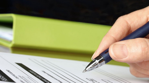 Hand with Pen Signing Form by Green Folder