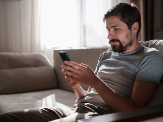 Portrait of an attractive smiling young bearded man wearing casual clothes sitting on a couch