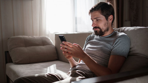 Portrait of an attractive smiling young bearded man wearing casual clothes sitting on a couch