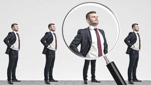 Businessmen on conveyor, magnifying glass