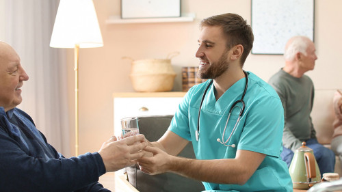 Care worker giving water to elderly man in geriatric hospice. Ba