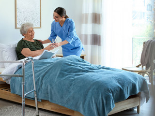 Care worker giving water to elderly woman in geriatric hospice