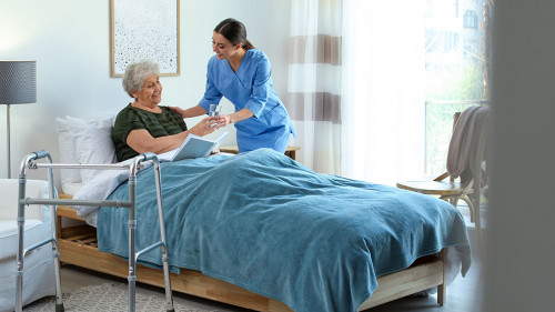 Care worker giving water to elderly woman in geriatric hospice