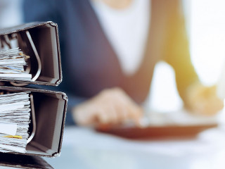 Binders with papers are waiting to be processed by business woman or bookkeeper working at the desk in office back in blur. Audit and tax concept