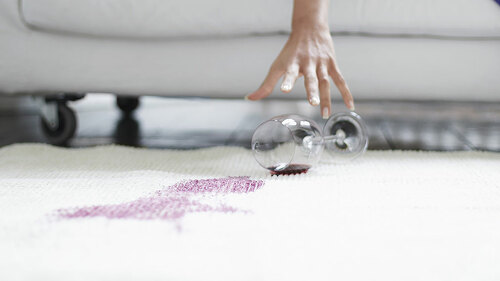 Midsection of woman reaching toward spilled wine glass on rug