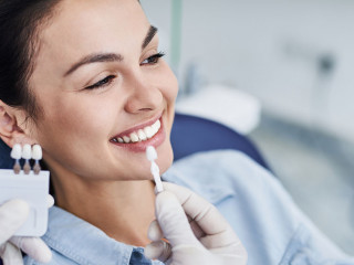 Male dentist comparing color of lady teeth with sample