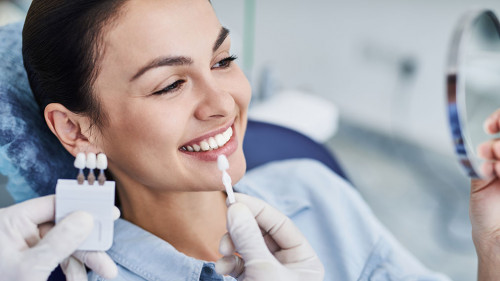 Male dentist comparing color of lady teeth with sample