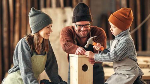 Kid with parents assembling wooden bird house in craft workshop