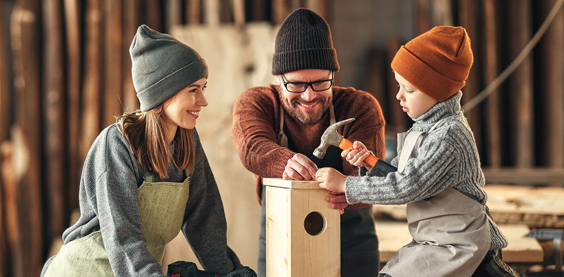 Kid with parents assembling wooden bird house in craft workshop