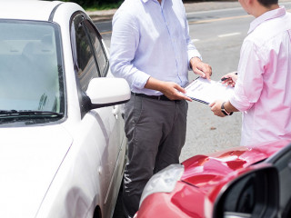 Insurance agent writing on clipboard while examining car after a
